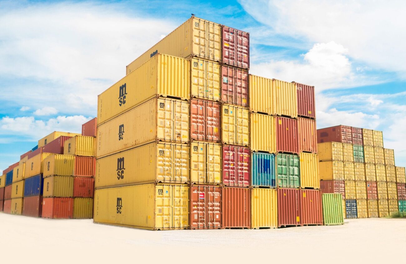 Stacks of colourful shipping containers arranged in rows under a bright blue sky, symbolising global trade and logistics.