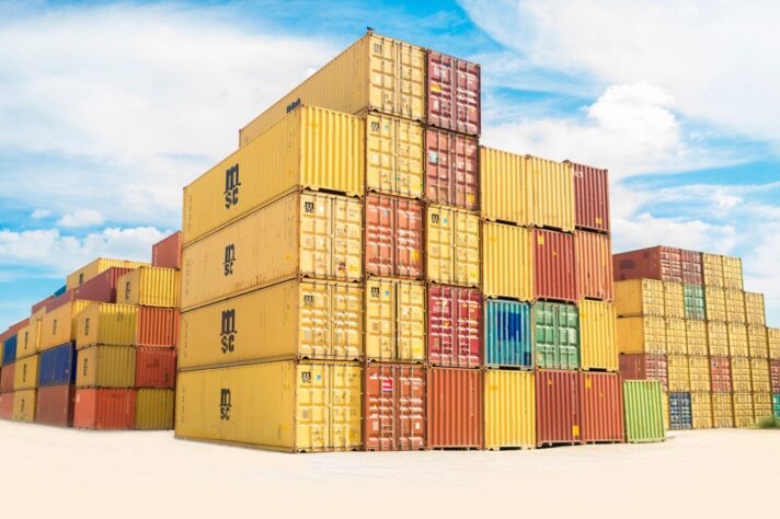 Stacks of colourful shipping containers arranged in rows under a bright blue sky, symbolising global trade and logistics.